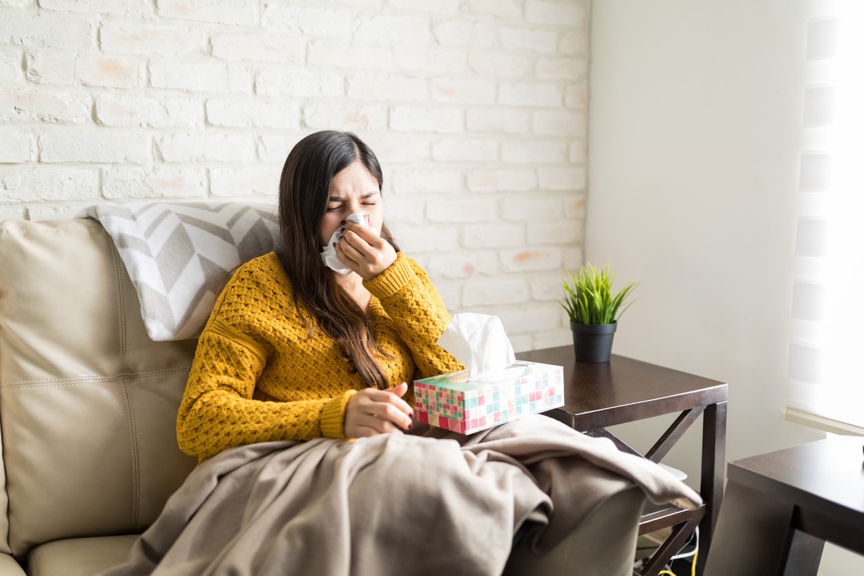 Sick woman blowing her nose in a tissue at home.