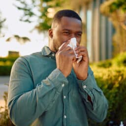 Man blowing his nose with a tissue outdoors