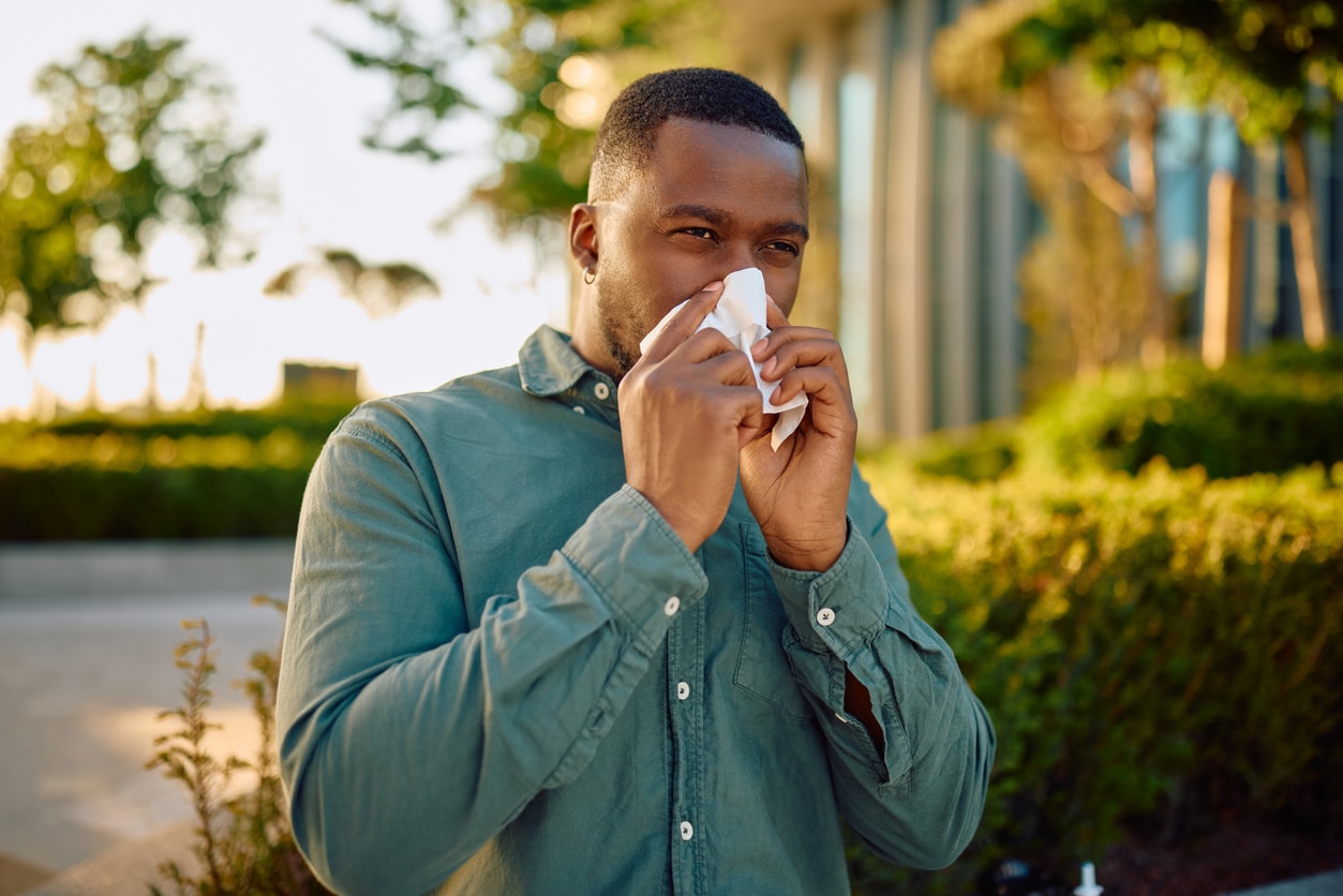 Man blowing his nose with a tissue outdoors.