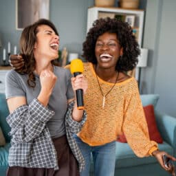 Two female friends singing karaoke at home