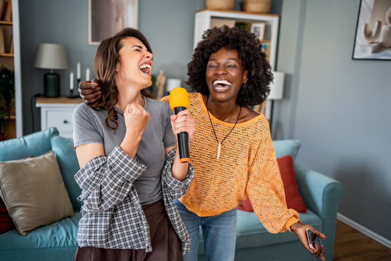 Two female friends singing karaoke at home.