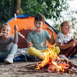 Group of young friends camping and burning a wood fire, toasting marshmallows over a fire.