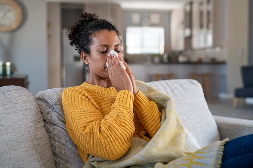 Young woman sneezing into a tissue at home.